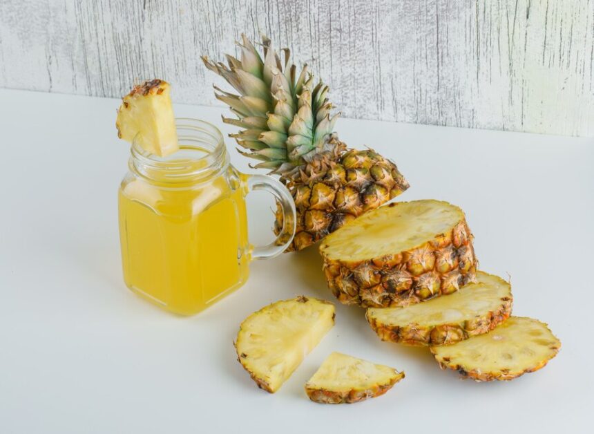 A glass of pineapple juice and some sliced pineapples 