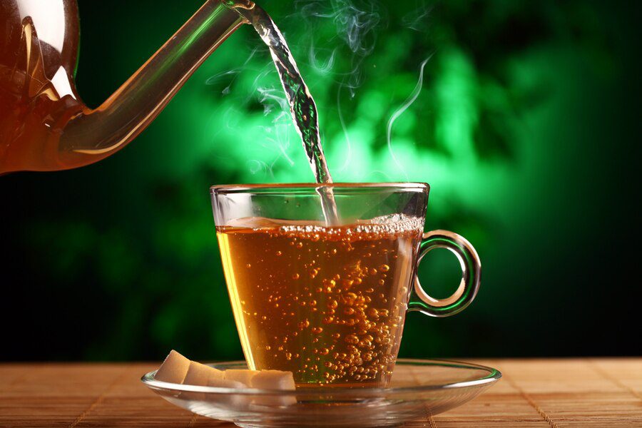 An image showing hot green tea being poured into a cup. Green tea is  a part of healthy foods