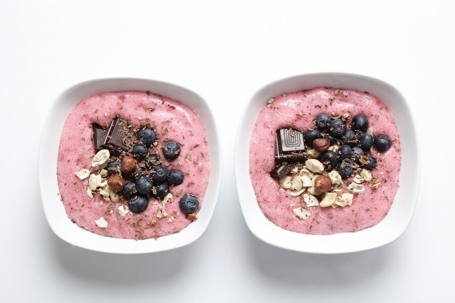 Two bowls of yoghurt with nuts,dark chocolates and berries as toppings. one of the healthy foods a person can eat