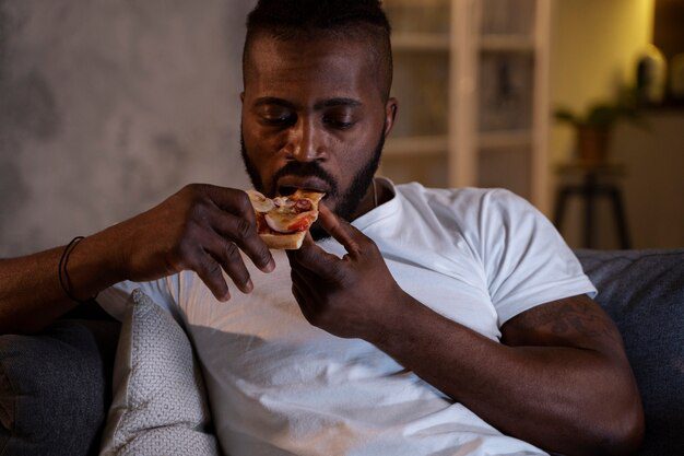 A man eating a slice of pizza, and is probably malnourished. 