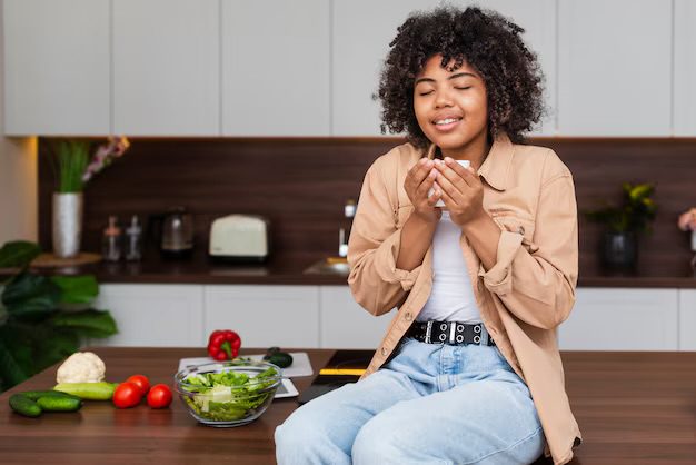 A lady sitting on her kitchen counter, smelling a bowl of food. She is also practicing mindful eating.