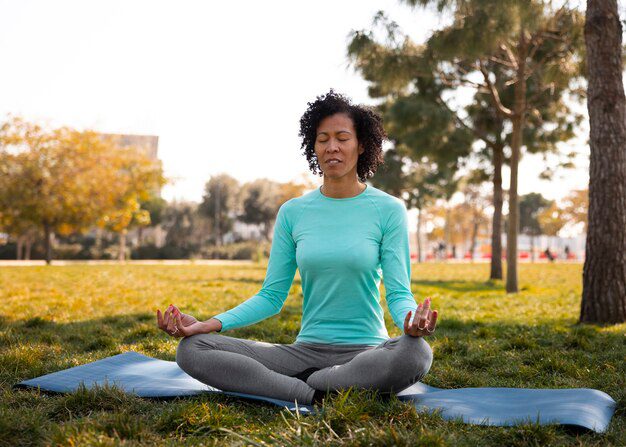 A lady outside on a mat meditating to practicing holistic health. 