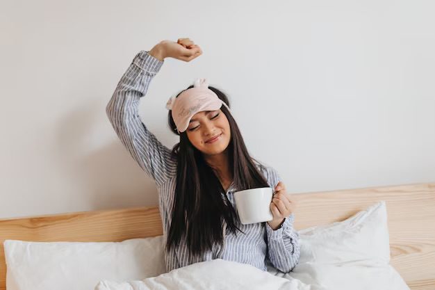 Natural remedies for better sleep. A lady in bed after waking up with a cup of tea in her hand. 