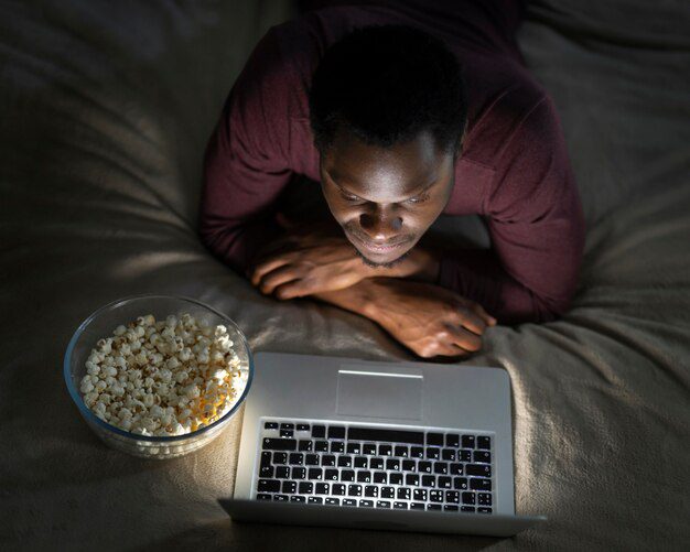 Technology on sleep quality. A man watching a content on his laptop, while laying on his bed with a bowl of popcorn.